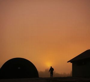 Silhouette man walking by built structure against sky during sunset