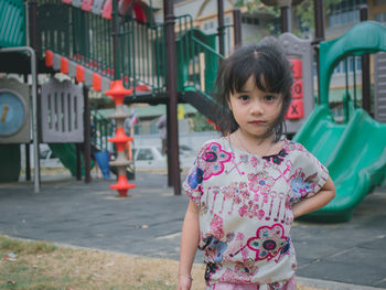 Portrait of cute girl standing against slide in playground