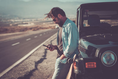 Side view of man using mobile phone by car