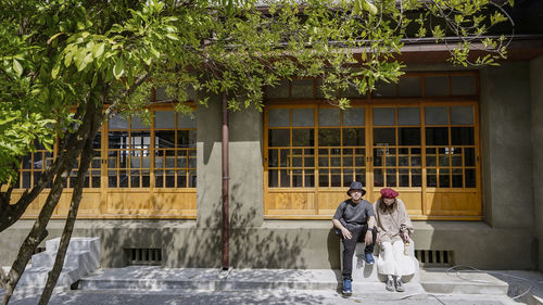 Full length of a couple sitting against building