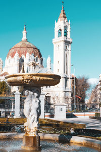 Statue by fountain against building in city against sky