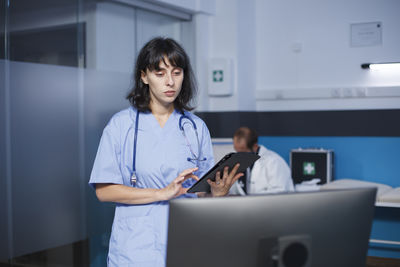 Portrait of young woman using mobile phone while standing in office