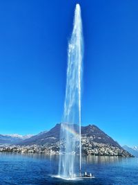 Fountain in lake against clear blue sky