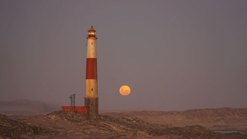 Lighthouse by sea against clear sky at night