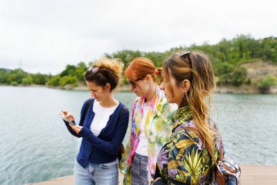 Young woman using phone while standing on lake