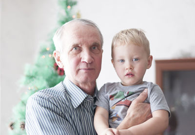 Portrait of grandfather holds his grandson in his arms and both laugh, the christmas tree