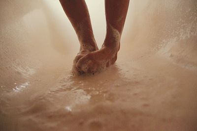 Low section of person standing on wet sand