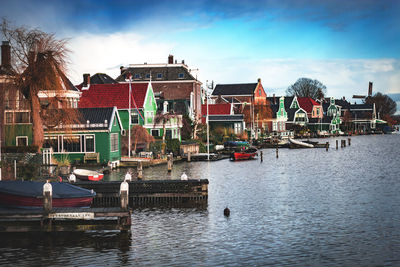 Sailboats moored on river by buildings against sky