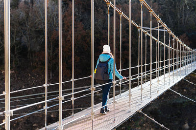 Rear view of woman crossing a high suspension bridge