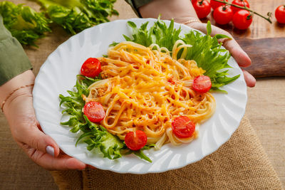 A plate of pasta with cherry tomatoes and cheese in female hands. horizontal photo
