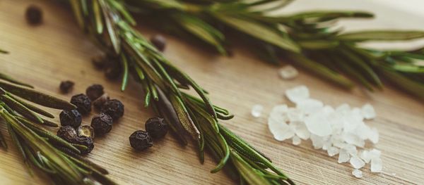 Close-up of rosemary and black peppercorns with salt on table