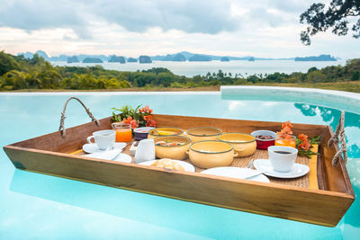 Lounge chairs and table at swimming pool against sky