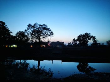 Silhouette trees by lake against sky at sunset