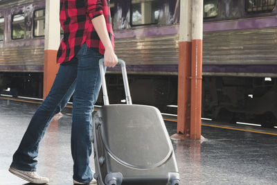 Low section of woman pulling wheeled luggage at railroad station