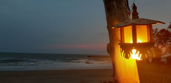 Illuminated lamp post on beach against sky during sunset