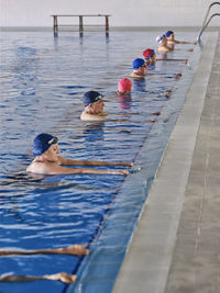 Group of people in swimming caps standing in pool during water aerobics class