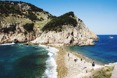 People on rocky shore against clear sky