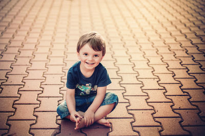 Portrait of smiling boy sitting on footpath