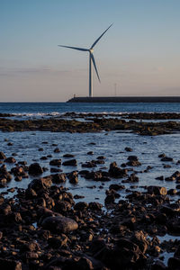 Traditional windmill by sea against sky during sunset