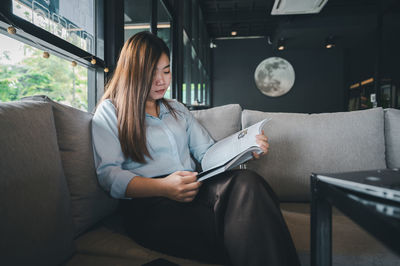 Midsection of woman holding paper while sitting on sofa