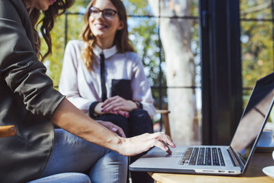 Midsection of woman using laptop computer while sitting with colleague in cafe