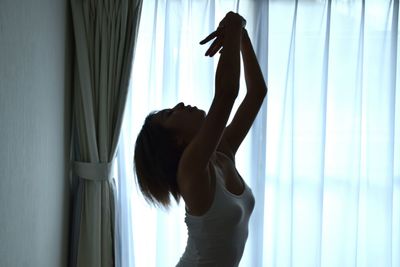 Close-up of woman dancing against curtain at home