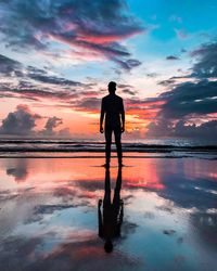 Rear view of silhouette man standing at beach during sunset