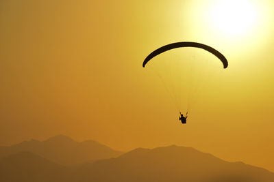Silhouette person paragliding against sky during sunset