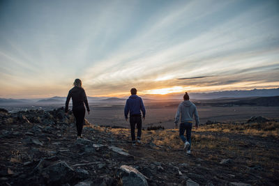 People standing on landscape against sky during sunset