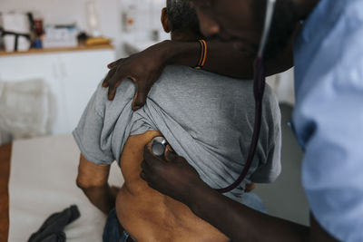 Male doctor checking senior man's back with stethoscope in examination room at clinic