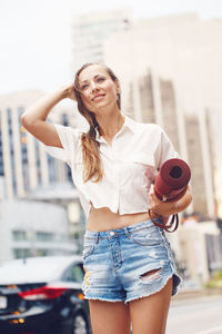Low angle view of beautiful woman holding exercise mat while standing in city