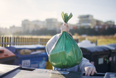 Man walking with rubbish. hand carrying plastic bag against garbage cans on street.