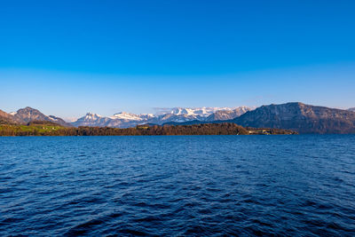 Scenic view of sea and mountains against clear blue sky