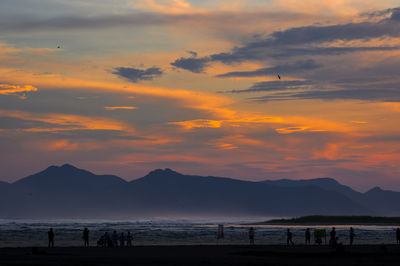 Silhouette people on beach against sky during sunset