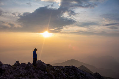 Man standing on rock against sky during sunset