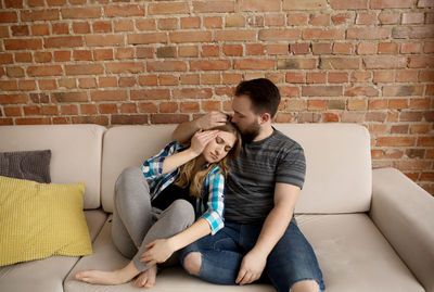 Young couple sitting on sofa against brick wall