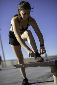 Woman tying shoelace against blue sky