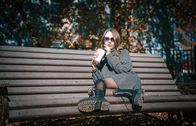Portrait of young woman sitting on bench in park