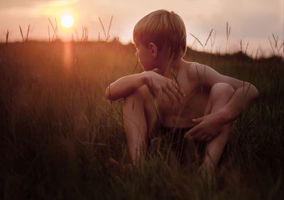 Side view of shirtless boy sitting on grassy field