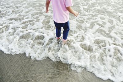 Low section of child standing on shore at beach