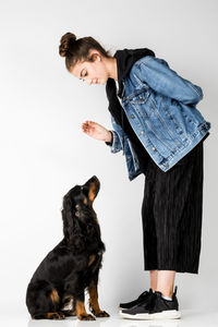 Full length of young woman playing with puppy against white background