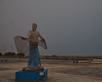 Man standing by statue against sea against clear sky during sunset