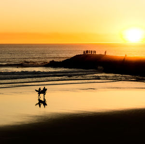 Silhouette people on beach against sky during sunset