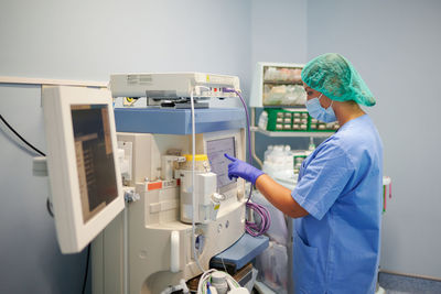 Side view of anonymous female medic in uniform touching monitor of medical equipment in clinic