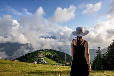 People walking on grassy field against cloudy sky