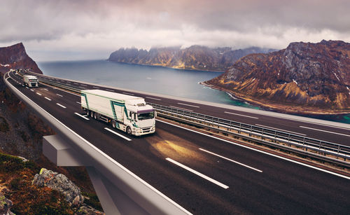 Truck on bridge over sea against cloudy sky