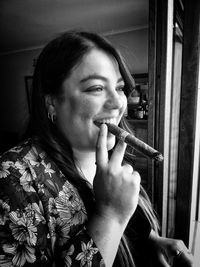 Smiling young woman smoking cigar at home