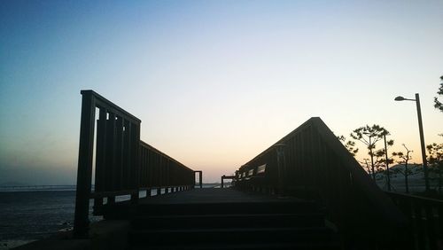 Silhouette bridge over sea against clear sky during sunset