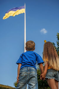 Girl in yellow and boy in blue look at biggest national flag of ukraine. pray for peace and victory