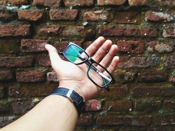 Close-up of hand holding eyeglasses against brick wall